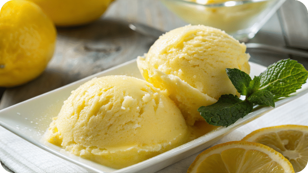 Bright yellow lemon sorbet served in scoops on a white plate, garnished with lemon slices and a sprig of mint.